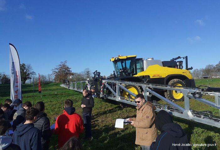 public de jeunes et technicien agricole devant u tracteur muni d'un épandeur de produits de traitements phytosanitaires